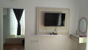 A room with a mounted TV on a white wall, a small shelf below it, and a mirror on the right. - Captain's Cabin Resort  (Kota Bharu)