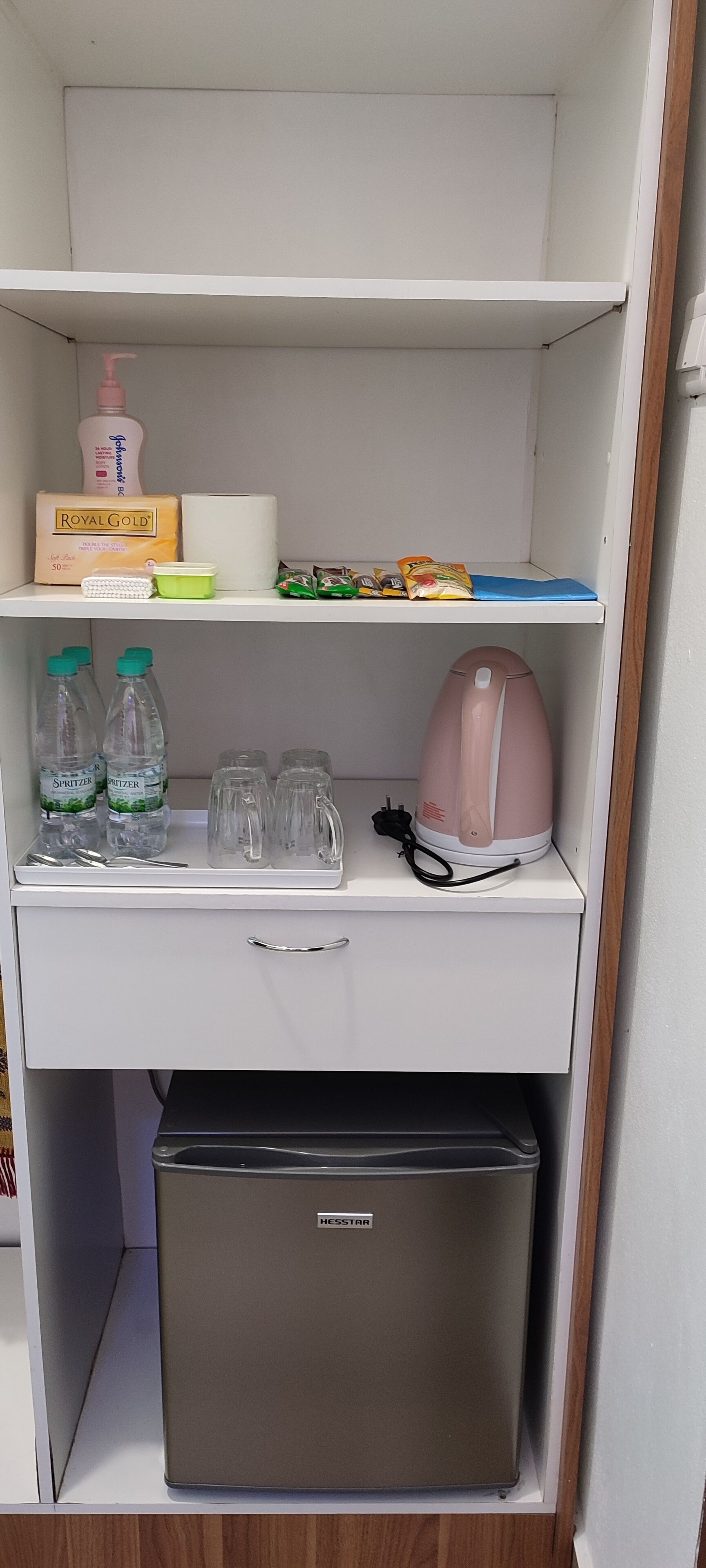 A kitchenette with a refrigerator, a kettle, bottles, and some food items.