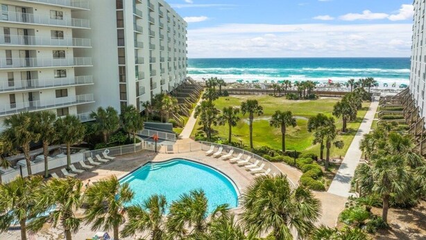 Um hotel com piscina, palmeiras e vista para o oceano.