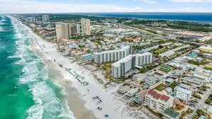 Vista aérea de uma cidade costeira com praia, edifícios altos e céu claro.