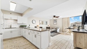 Uma cozinha moderna com armários brancos, uma ilha central e uma área de jantar com mesa e cadeiras.