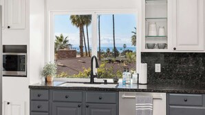 A kitchen with a view of palm trees and the ocean, a black faucet, and a microwave.