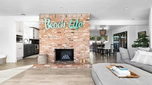 A modern living room with a brick fireplace, a sofa, and a dining area in the background.