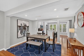 A modern kitchen with white cabinets, a dining area with a wooden table and chairs, and a blue patterned rug.