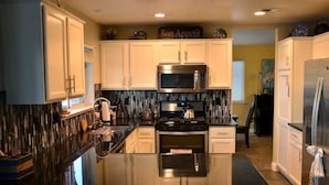 A modern kitchen with white cabinets, a central island, a stainless steel refrigerator, and a microwave.