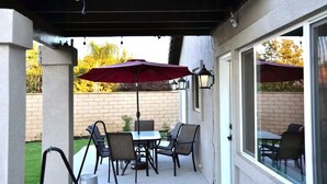 An outdoor patio with a table and chairs, a red umbrella, and a brick wall in the background.