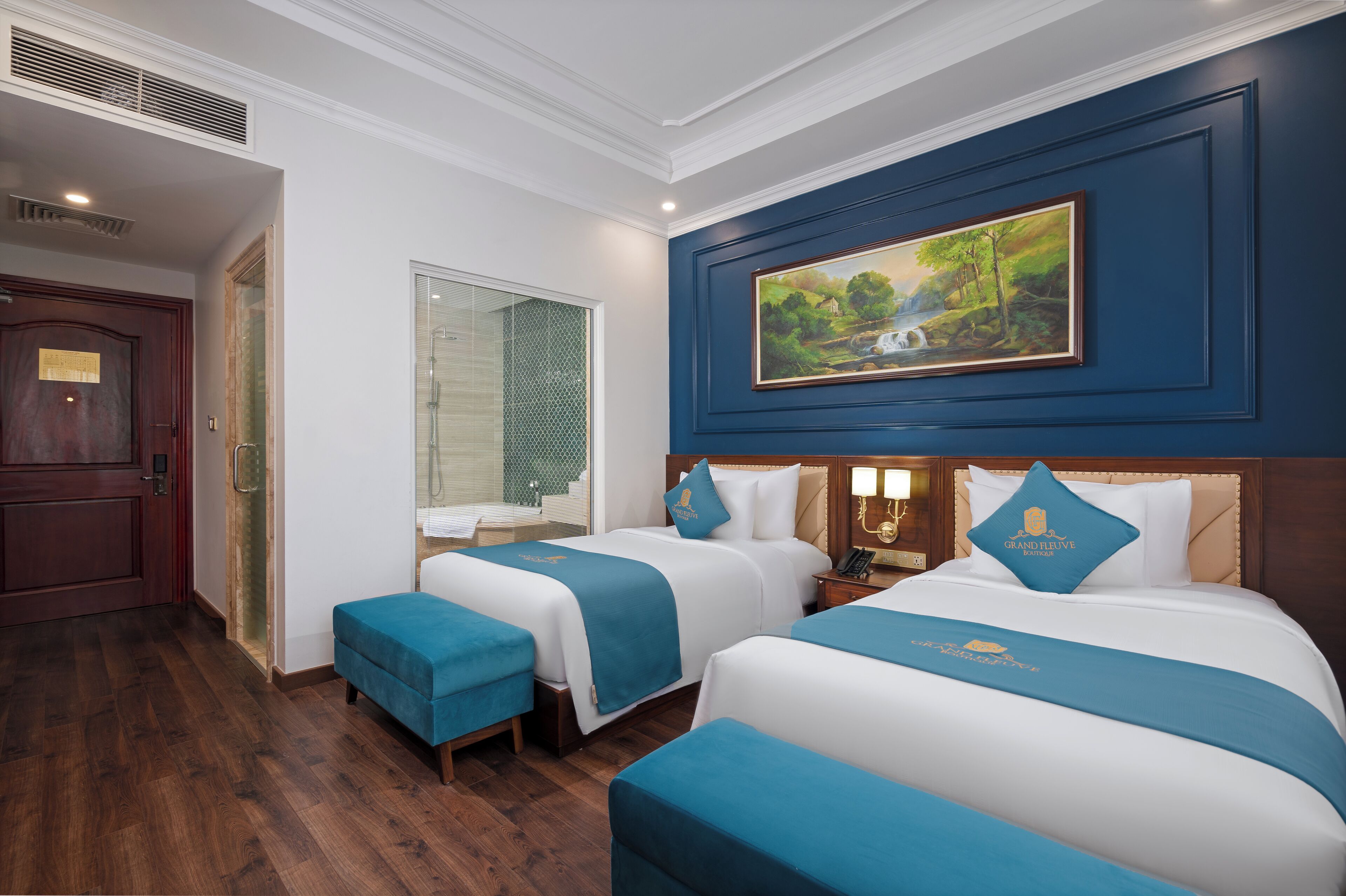 A hotel room with two beds, a painting, and a wooden door.