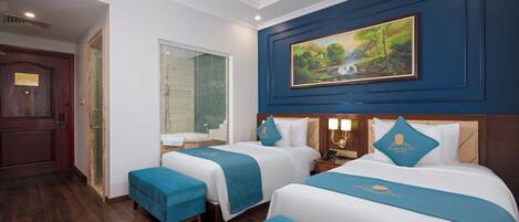 A hotel room with two beds, a painting, and a wooden door.