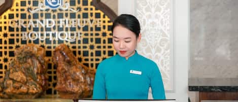 En receptionist vid hotellreceptionen, med en skylt i bakgrunden som visar texten ”GRAND FLUVE BOUTIQUE”.