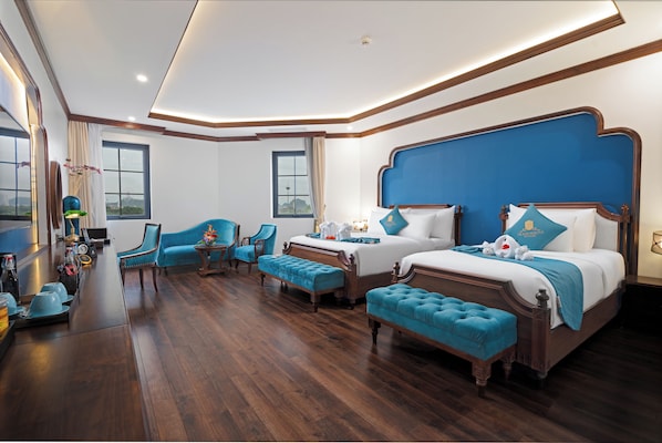 A spacious bedroom with a large bed, two smaller beds, a sitting area with chairs, and a wooden floor. - Grand Fleuve Boutique (Bai Chay)