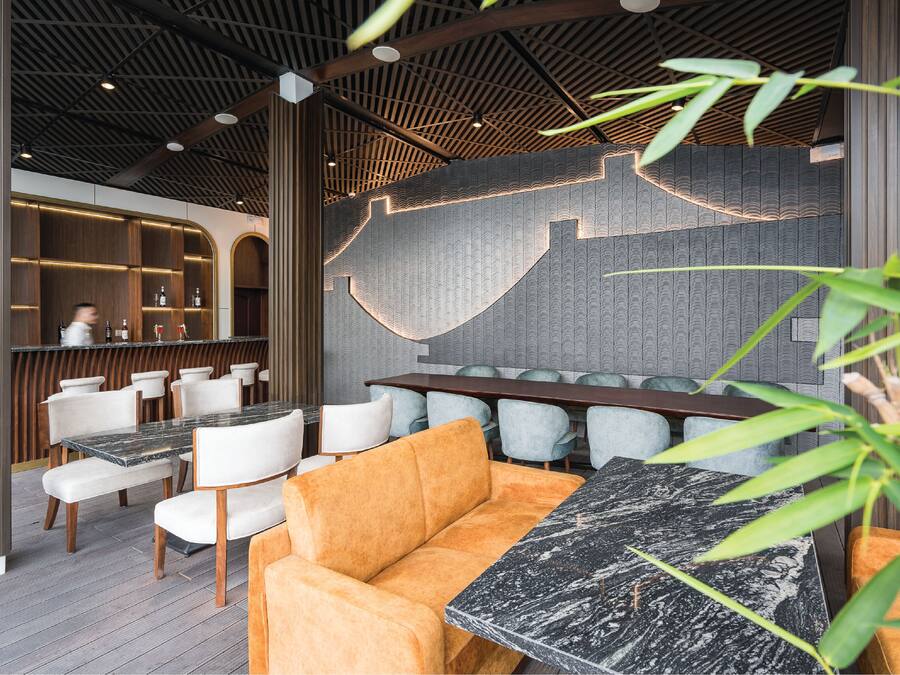 A modern restaurant interior with a wooden ceiling, seating arrangements, and a bar area.