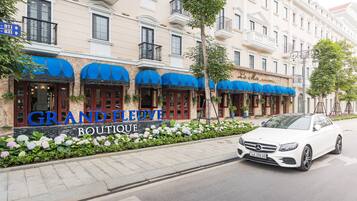 A building with a sign reading "GRANDELEUVE BOUTIQUE" and a white car parked in front.