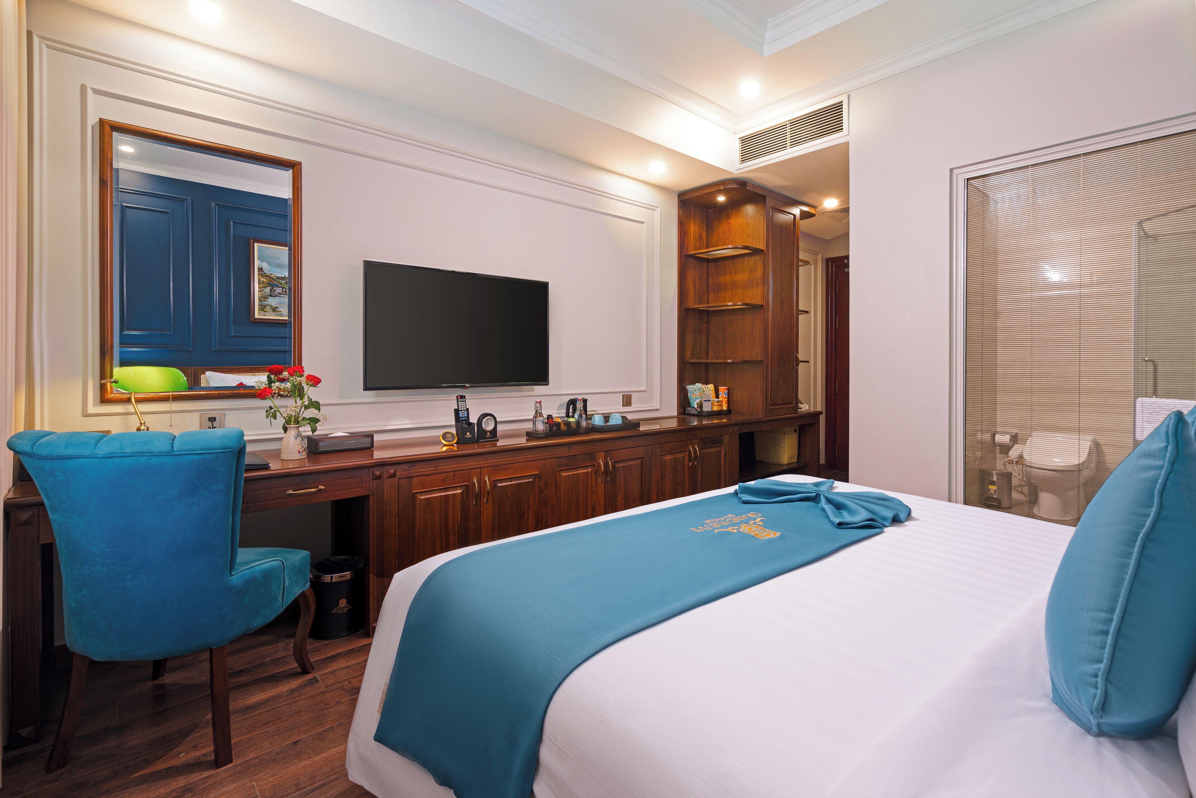 A hotel room with a bed, a desk, a chair, a television, and a bathroom with a shower and toilet.