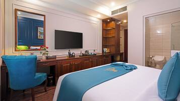 A hotel room with a bed, a desk, a chair, a television, and a bathroom with a shower and toilet.