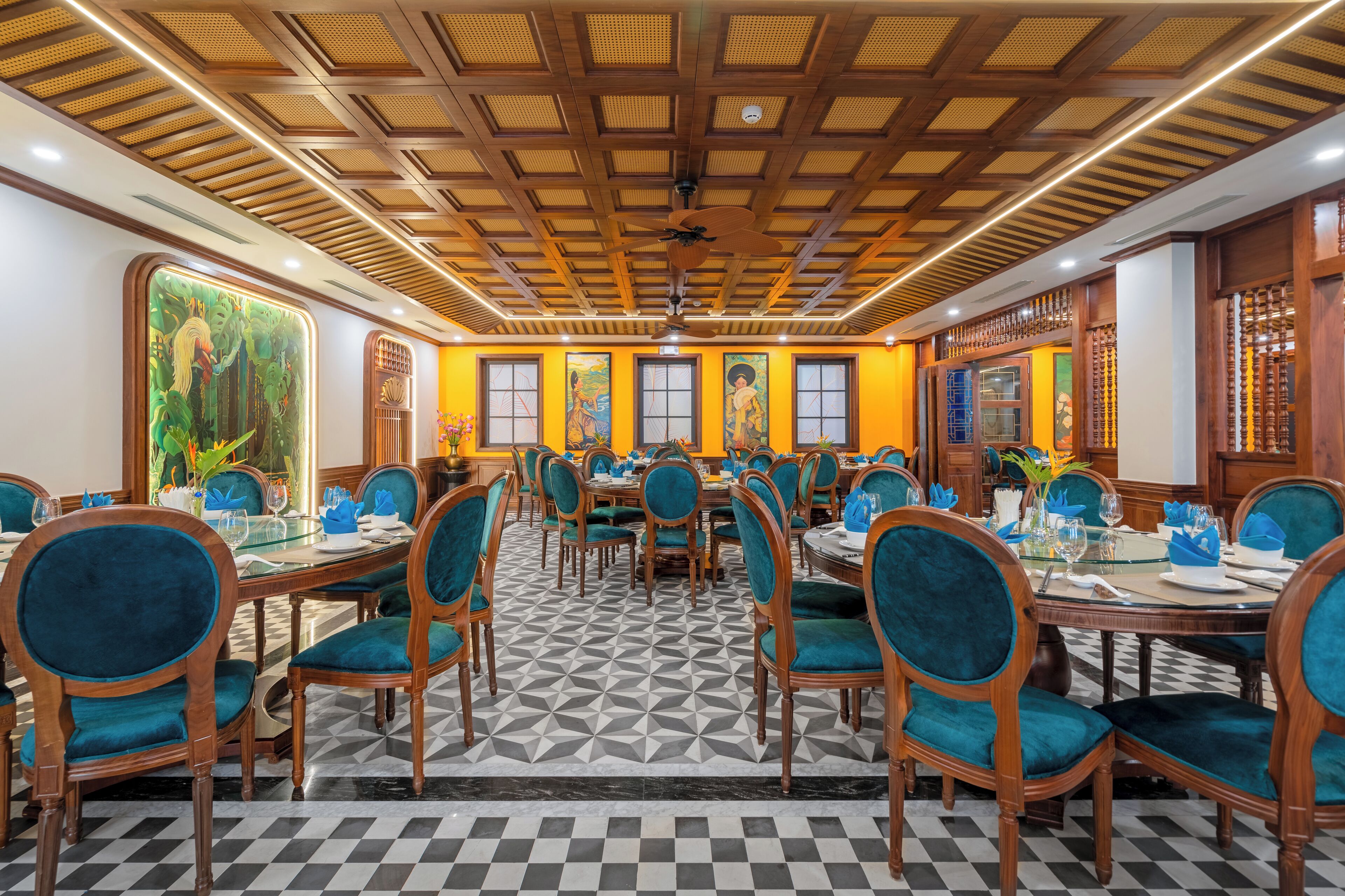 A spacious dining area with wooden tables and teal upholstered chairs, featuring a checkered floor and large windows with artwork.