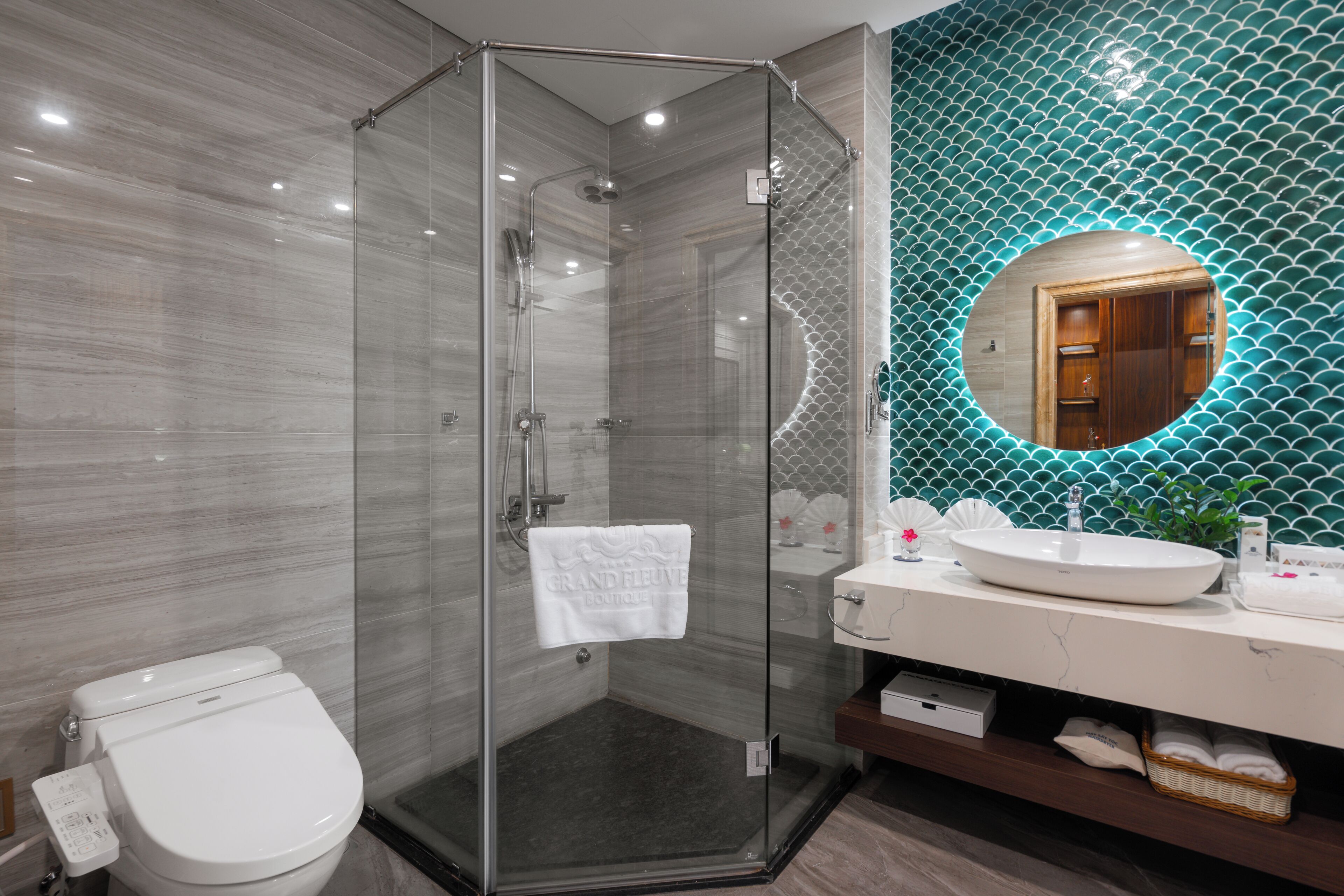 A modern bathroom with a glass-enclosed shower, a white toilet, a vanity with a sink, and a mirror with a circular frame.