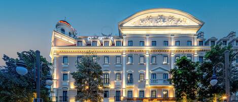 A grand hotel with classical architecture, multiple balconies, and a well-lit facade.