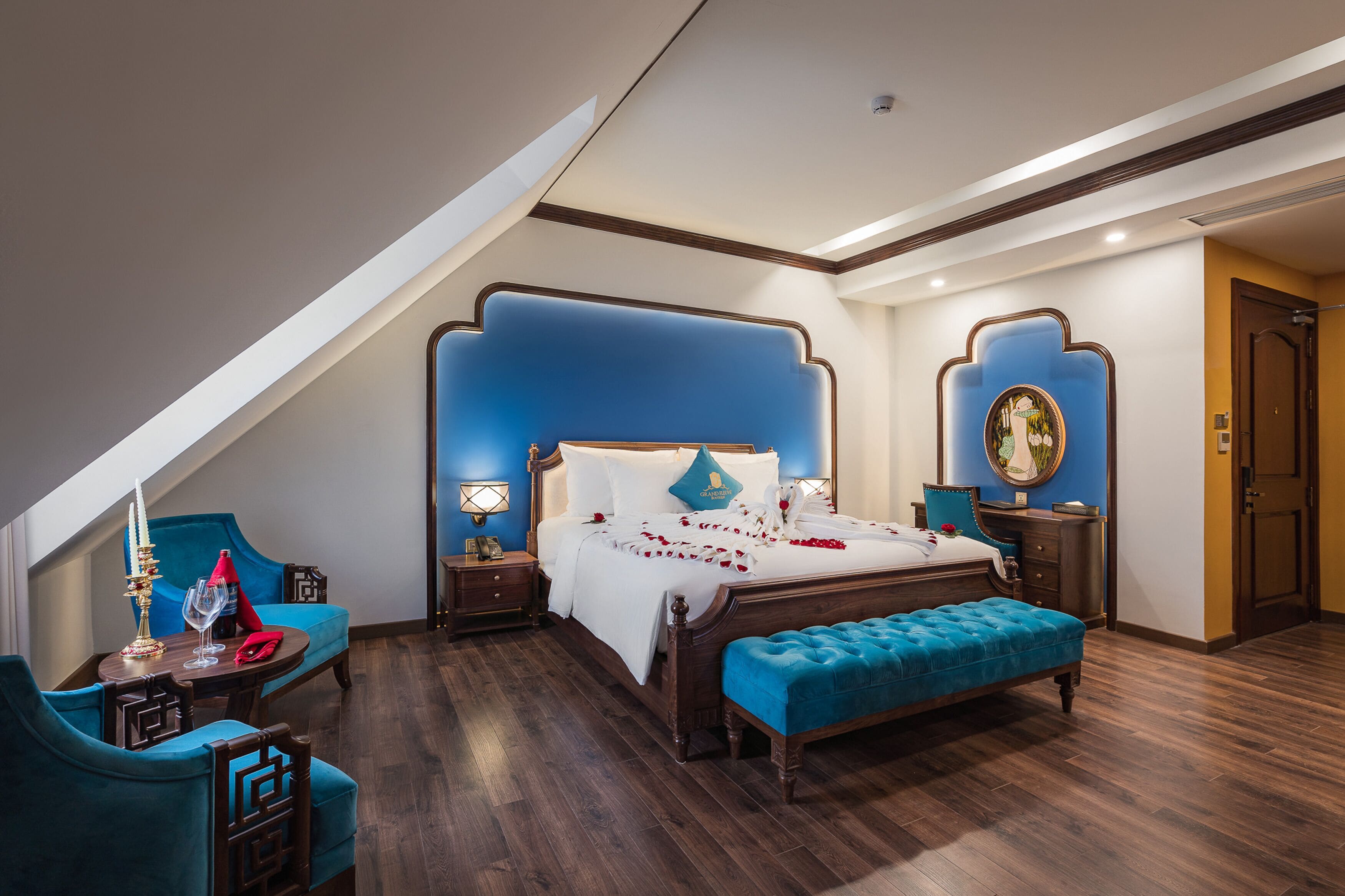 A bedroom with a large bed, a bench, a nightstand, a table, and a chair.