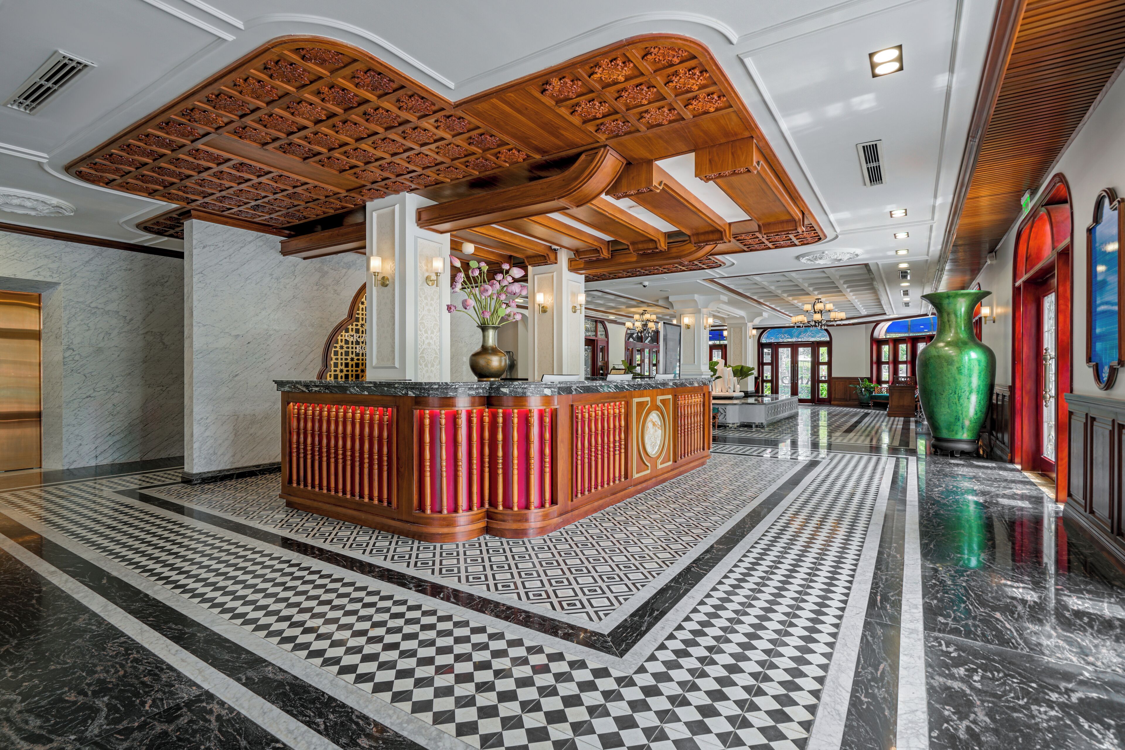 A lobby with a checkered floor, a central reception desk, and a large green vase.