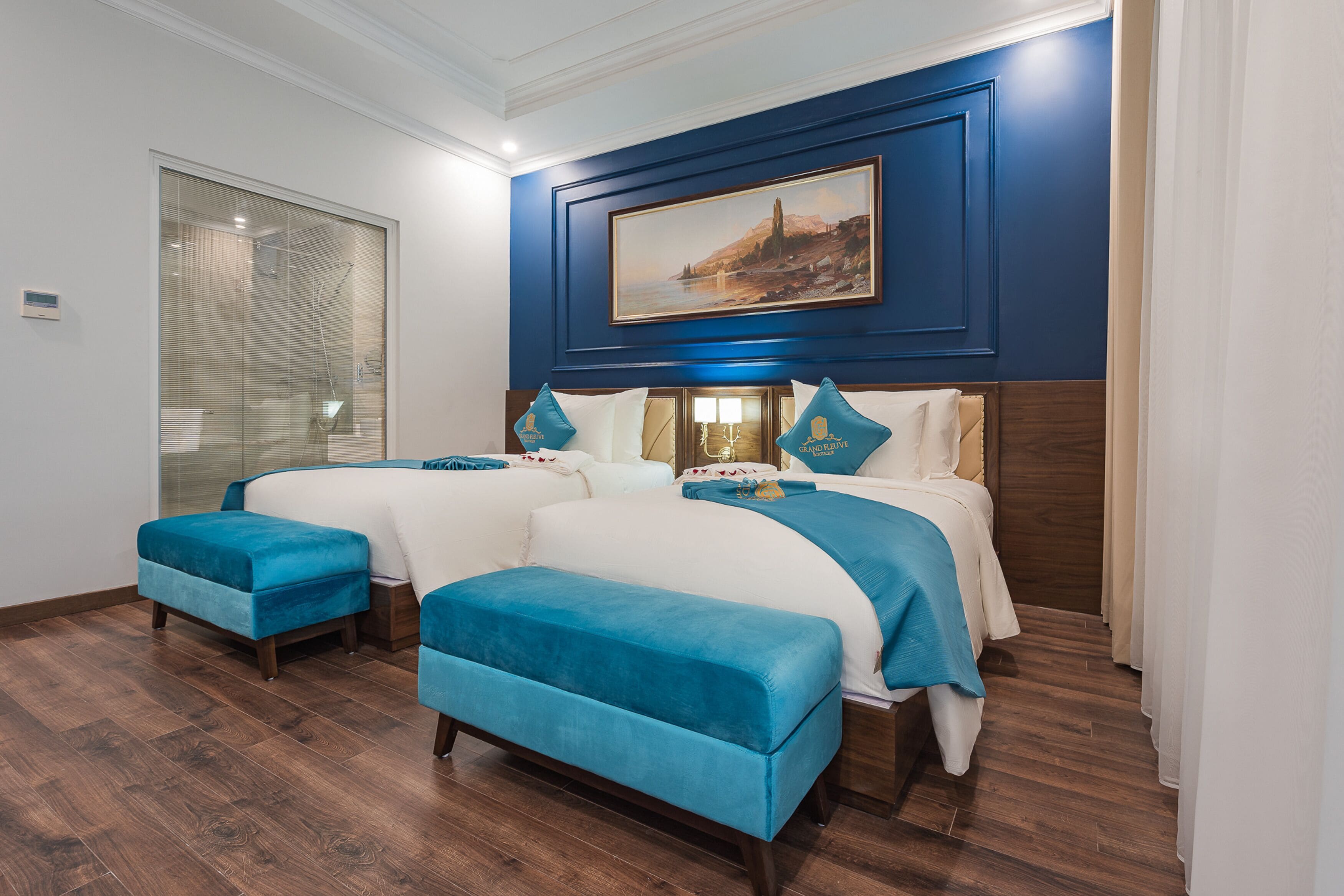 A hotel room with two beds, a large window, and a painting on the wall.
