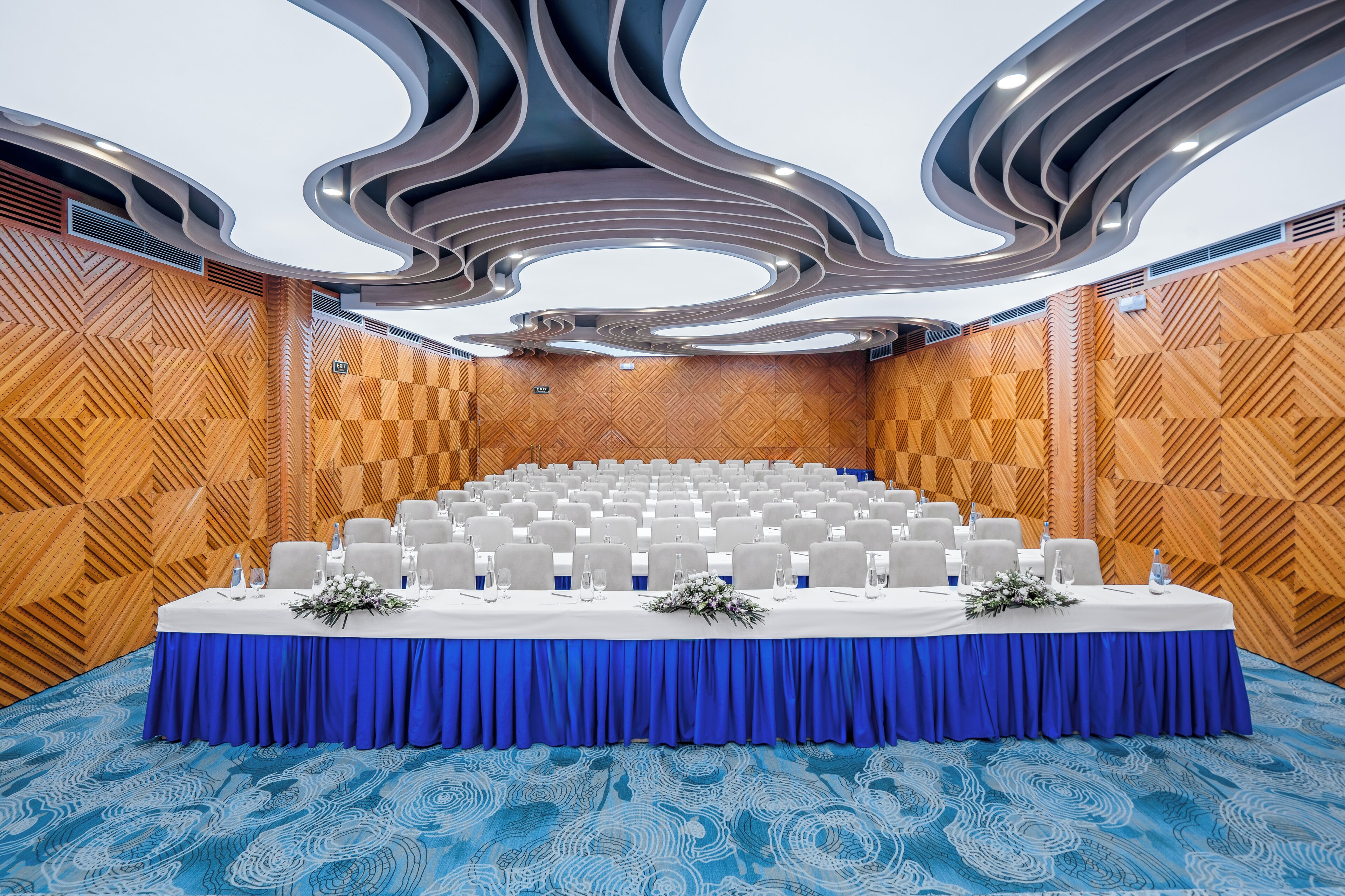 Un salón de conferencias con alfombra azul, mantel blanco y sillas grises.