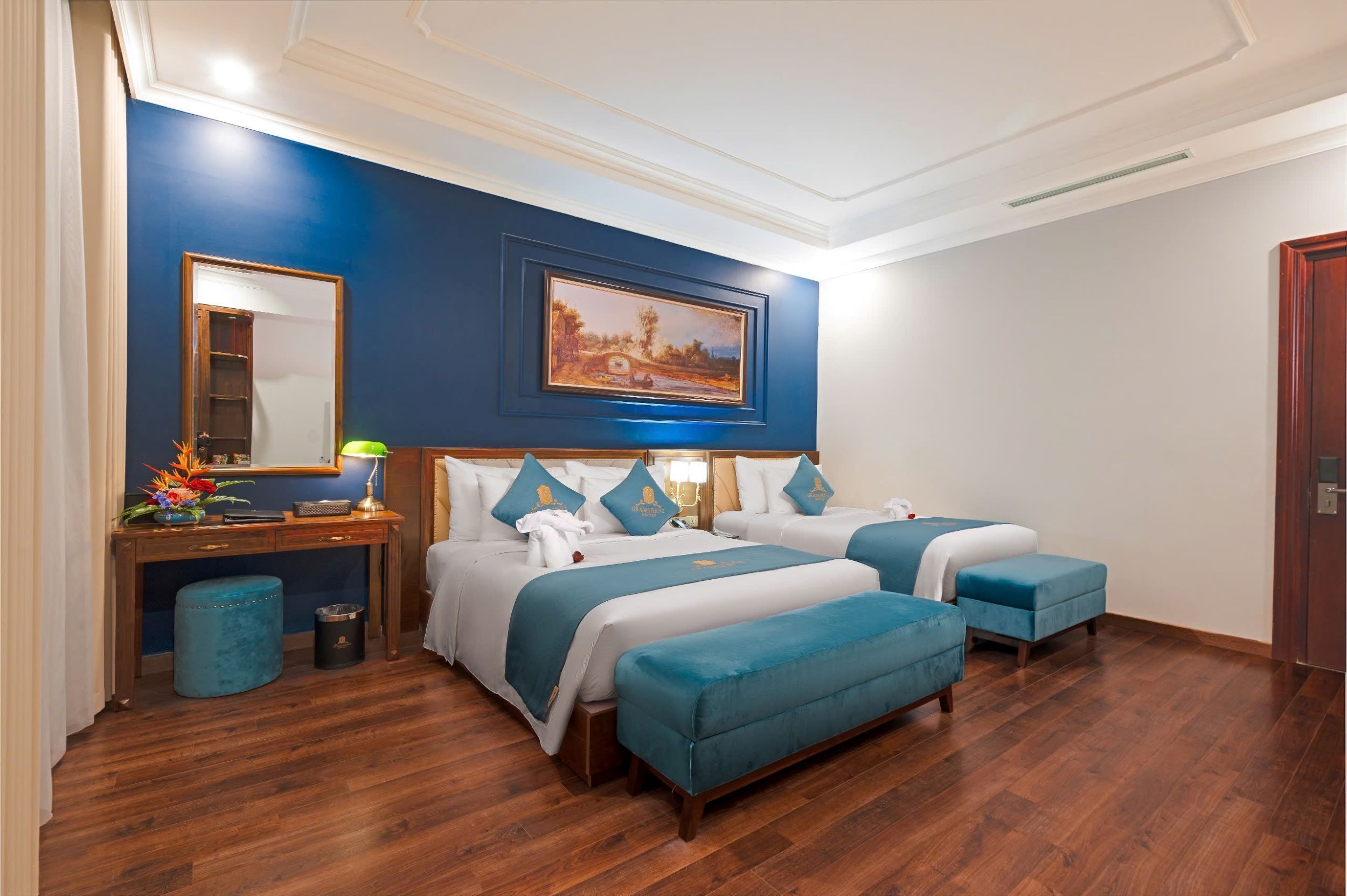 A hotel room with two beds, a desk, a mirror, and a painting on the wall.