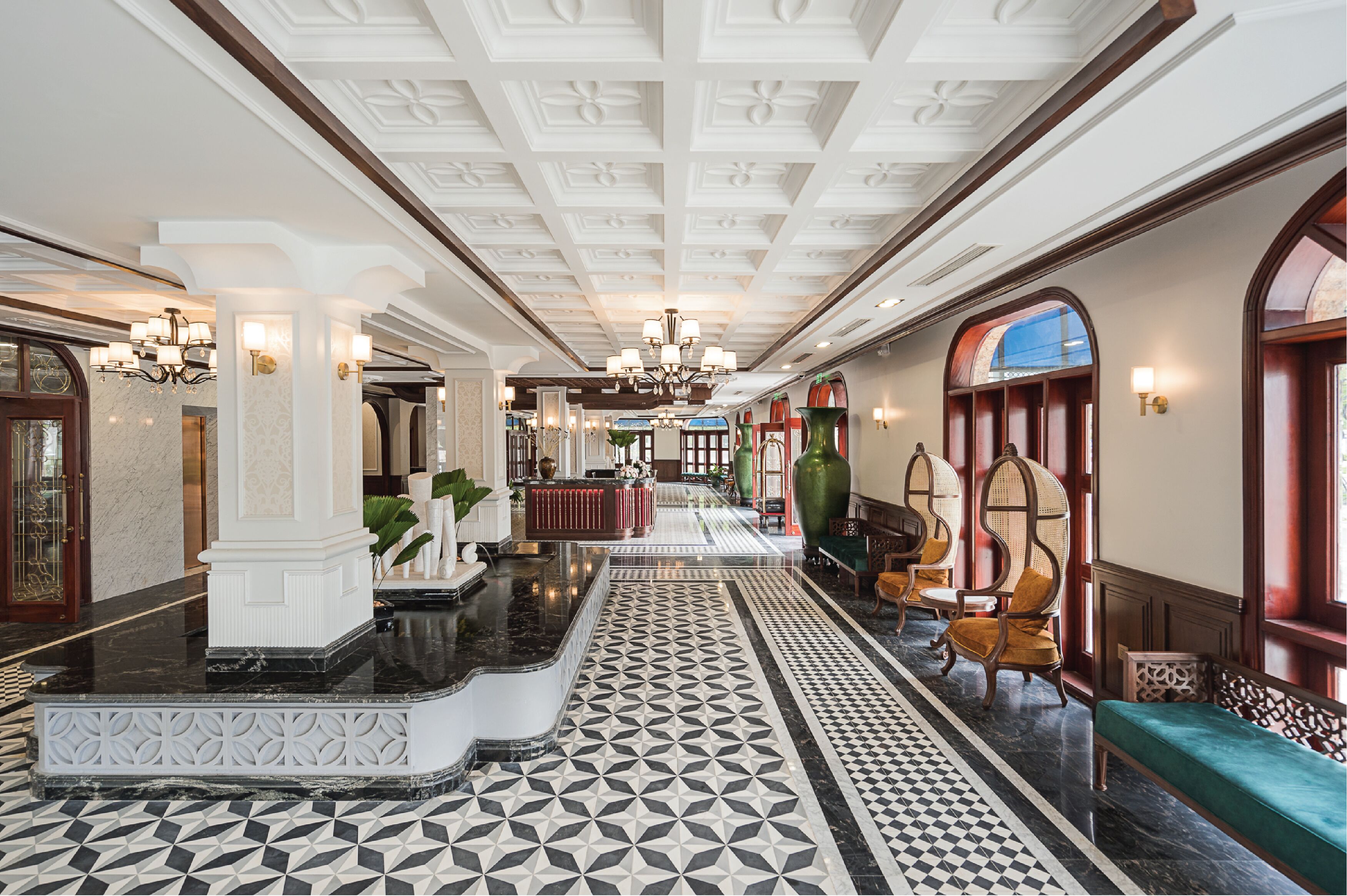 A grand lobby with a geometric patterned floor, a central reception desk, and classic furniture.