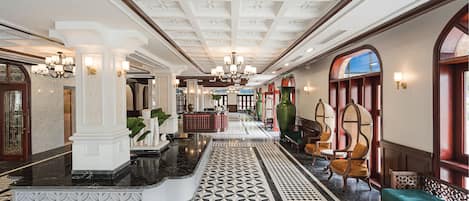 A grand lobby with a geometric patterned floor, a central reception desk, and classic furniture.