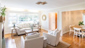 Ein geräumiges Wohnzimmer mit einer Couch, einem Couchtisch und Sesseln, ein Essbereich mit Tisch und Stühlen sowie ein großes Fenster, das für natürliches Licht sorgt.