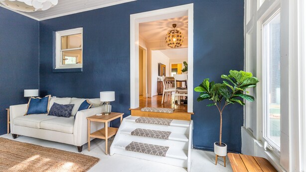 Ein Wohnzimmer mit blauer Wand, weißem Sofa und einer Treppe, die in einen Essbereich führt.