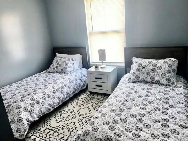 Une chambre avec deux lits simples, une table de chevet et une fenêtre avec des stores.