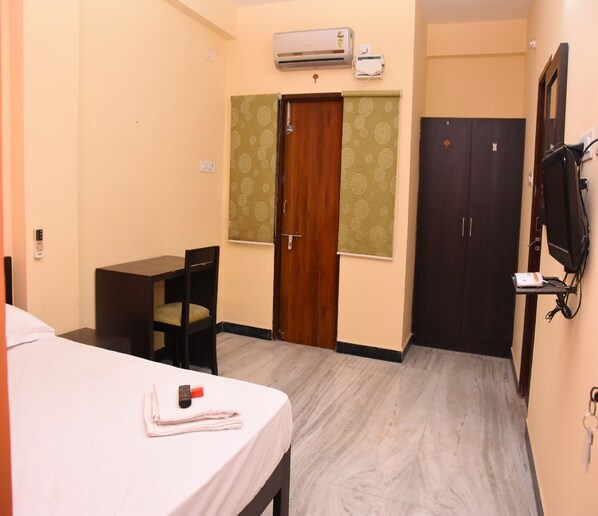 A hotel room with a bed, a desk, a chair, a wardrobe, and an air conditioning unit.