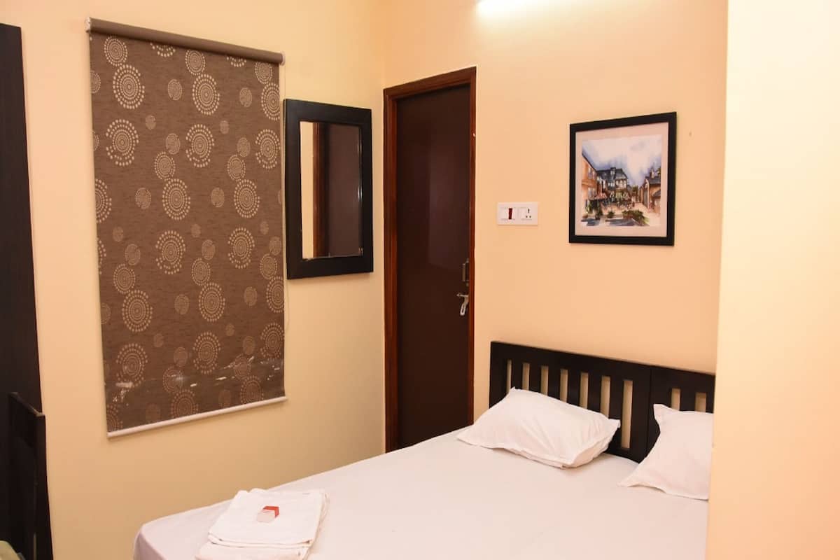 A neatly made bed with white linens, a brown patterned curtain, a framed picture on the wall, and a door with a wooden frame.