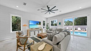 A modern living room with a large TV, comfortable seating, and a view of a pool. - Barton Vista Del Mar | Paradise Perfected!! | Deeded Access with Free Beach Chairs & Umbrellas 100 Yards Away! (Miramar Beach)