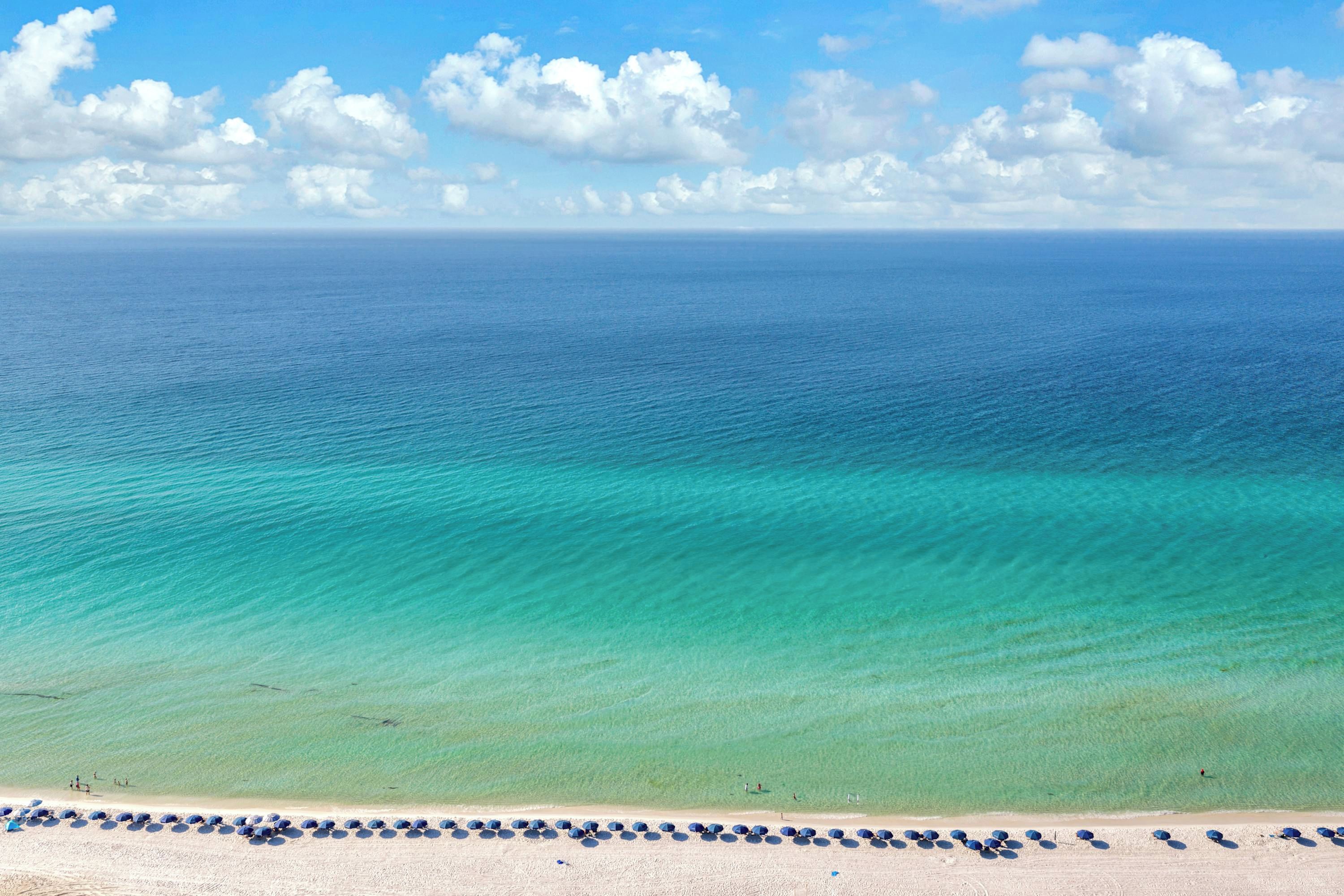 Une plage aux eaux turquoise et limpides, bordée d’une rangée de parasols.