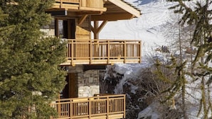 Una chaleta de madera de varios pisos con balcones, base de piedra y un telesilla al fondo.