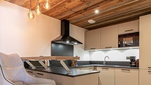 Una cocina moderna con techo de madera, una isla central, taburetes de bar y una campana extractora negra.