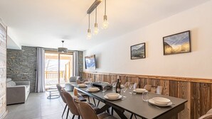 Comedor con una mesa larga dispuesta para seis personas, rodeada de sillas, con una pared de piedra y un panel de madera en el lateral.