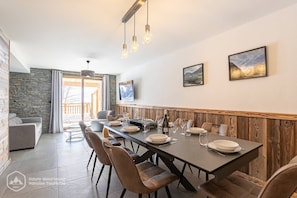 Ein Essbereich mit einem langen Tisch, gedeckt für sechs Personen, umgeben von Stühlen, mit einer Steinwand und einer Holzvertäfelung an der Seite.