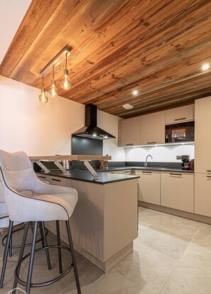 A modern kitchen with a wooden ceiling, a central island, bar stools, and a black range hood.