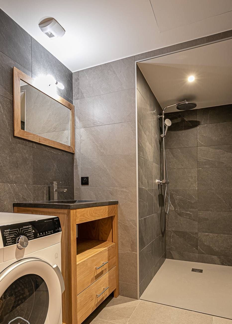 A modern bathroom with a built-in washing machine, a vanity with a mirror, and a walk-in shower.