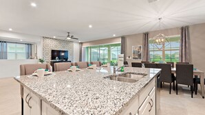 Eine moderne Küche mit einer großen Granitinsel, einem Essbereich mit Tisch und Stühlen sowie einer Wohnbereich mit Sofas und einem Fernseher.