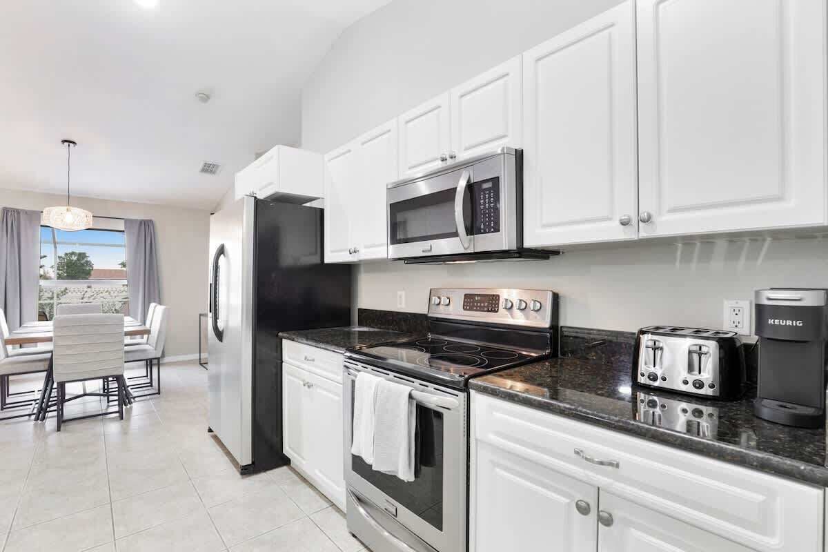 A modern kitchen with white cabinets, a stainless steel refrigerator, a microwave, a stove, a toaster, and a coffee maker.