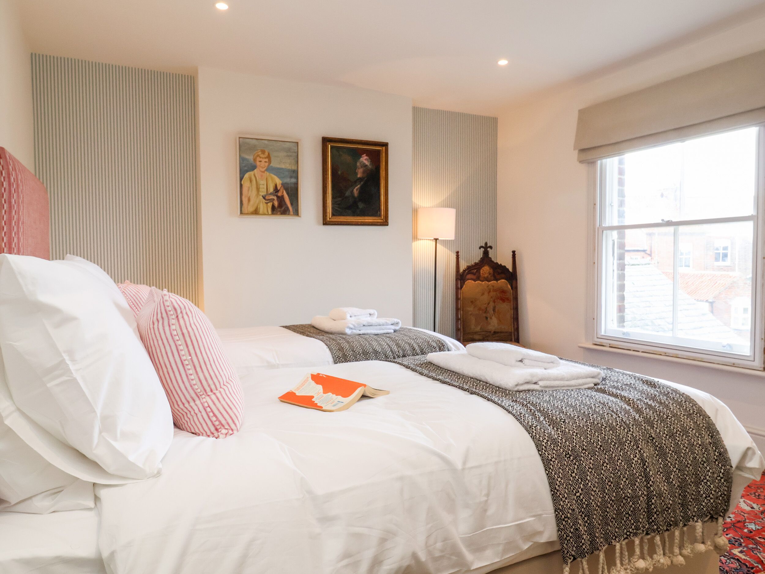 A hotel room with a large bed, a window with a view, a lamp, and two framed pictures on the wall.