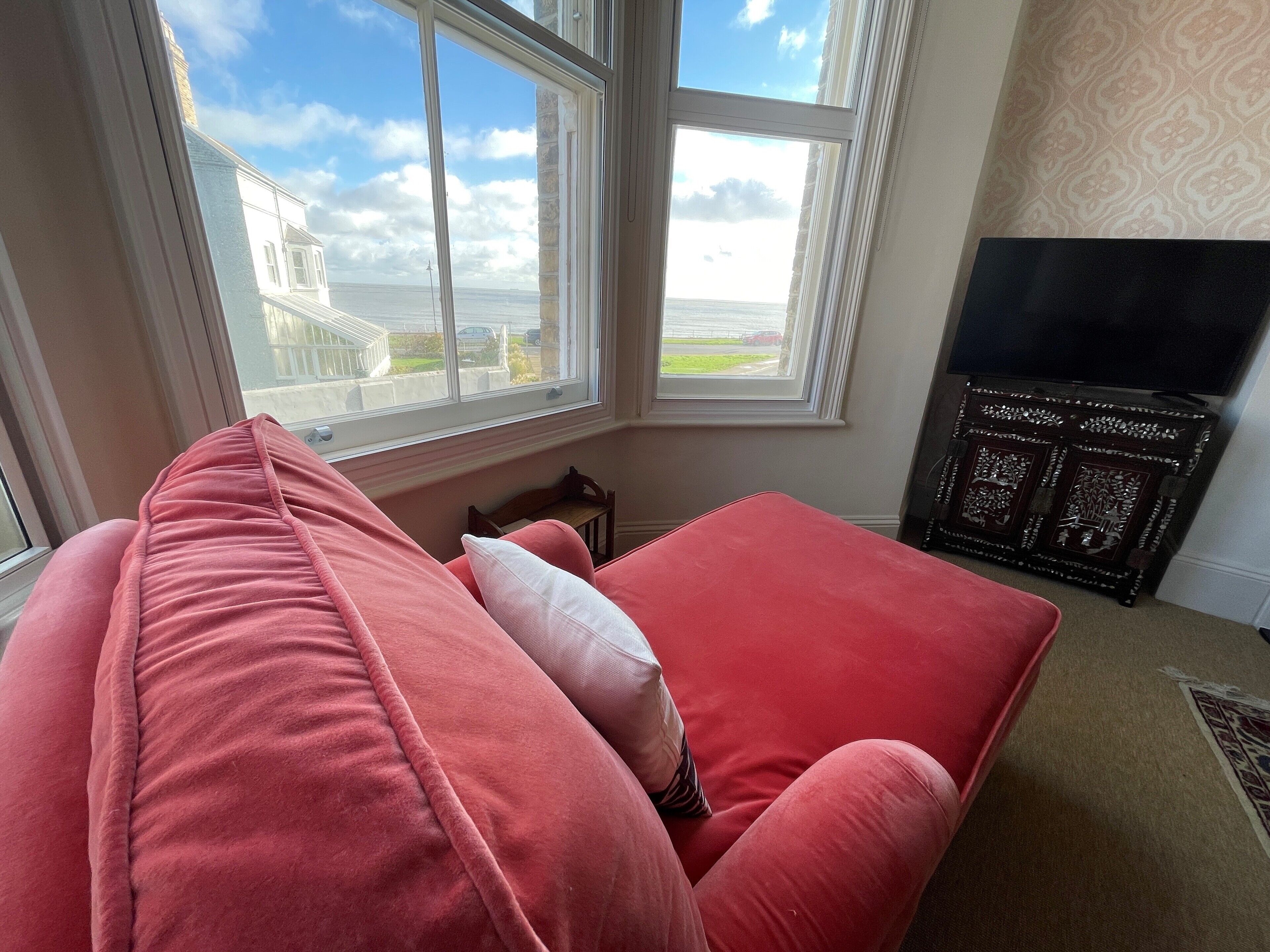 A living room with a red sofa, a television, and a view of the sea through large windows.