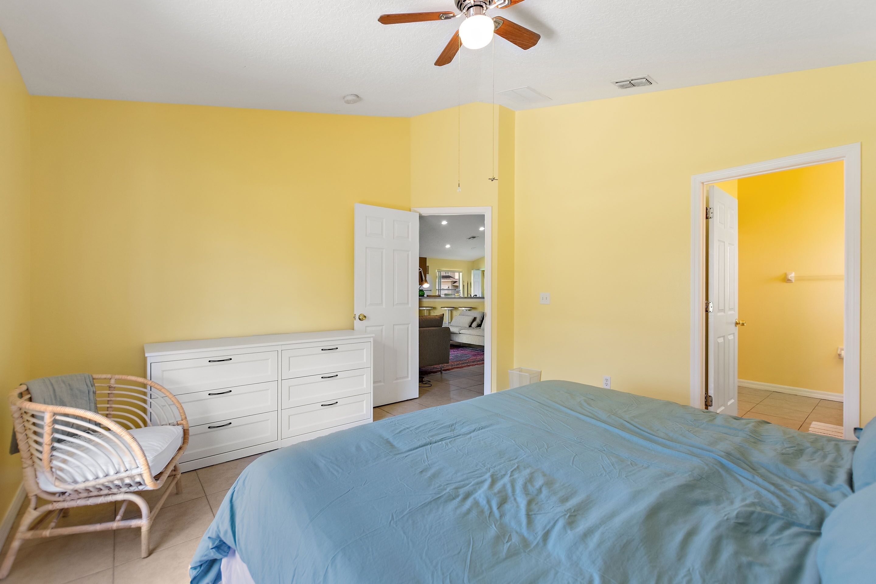 A bedroom with a bed, a dresser, a chair, and a ceiling fan.