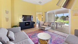 A living room with a sofa, a TV, a cabinet, and a colorful rug. - Gilded Parasol By Shine Villas Remington Golf #410 4 Bedroom Home (Kissimmee)