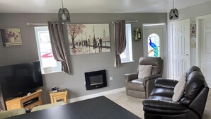 Ein Wohnzimmer mit Flachbildfernseher, Kamin, Ledersofa und großem Fenster mit Vorhängen.