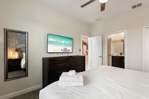 Un dormitorio con una cama grande, un aparador de madera oscura, un televisor montado en la pared y una puerta que da a un baño.