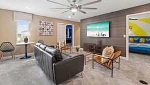 A modern living room with a leather sofa, glass coffee table, and a ceiling fan. - Marvel Mansion! Championsgate Resort Shine Villas 9 Bedroom Villa (Davenport)